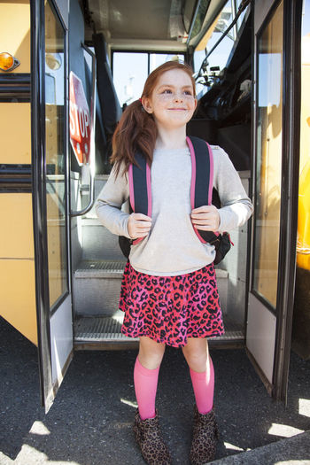 Happy girl with backpack at bus doorway