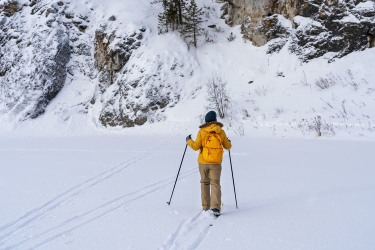 Rear view of young woman in yellow clothes with backpack skiing near rocks  winter sports hiking