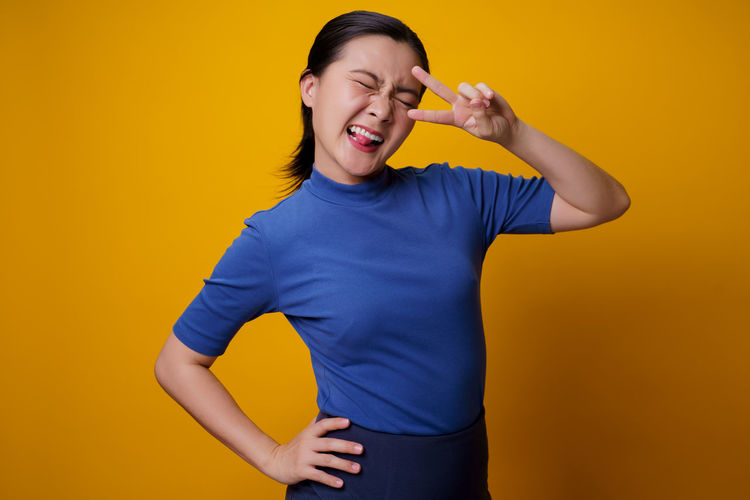 Smiling young woman holding yellow while standing against orange background