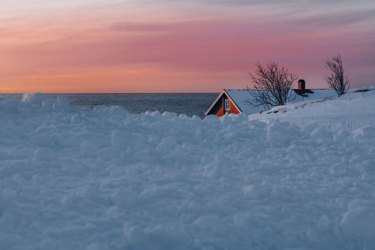 Snow covered land and sea against sky during sunset