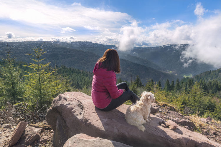 Rear view of woman with dog sitting on rock against mountains