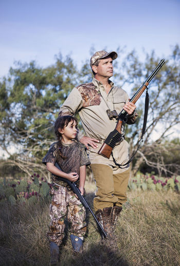 Hunters holding rifle and looking away while standing on grassy field