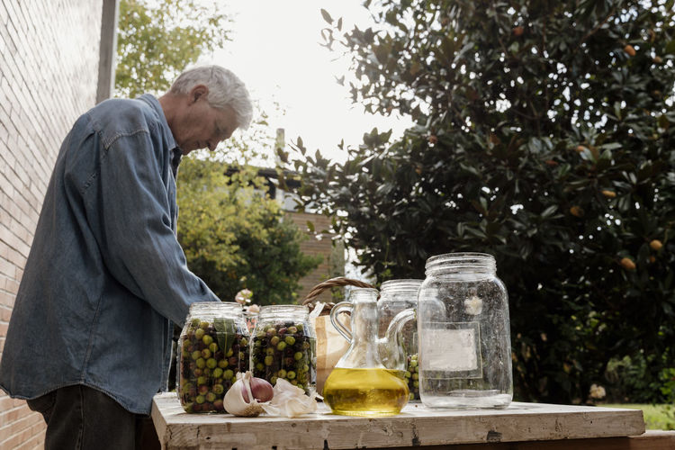 Senior man preparing olive pickle in glass jar on table in back yard
