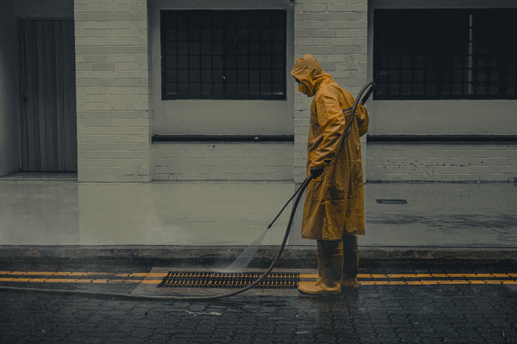 Cleaner washing the road on a rainy day in yellow rain coat attire