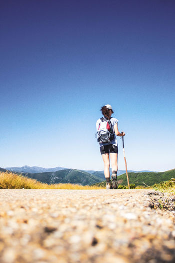 Woman hiking on road against mountain landscape and blue sky