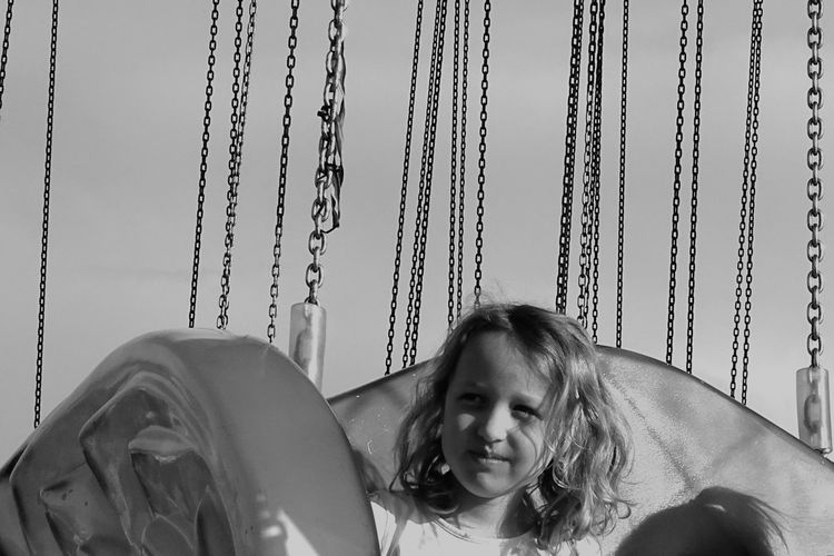 Cute girl looking away while sitting in carousel against sky