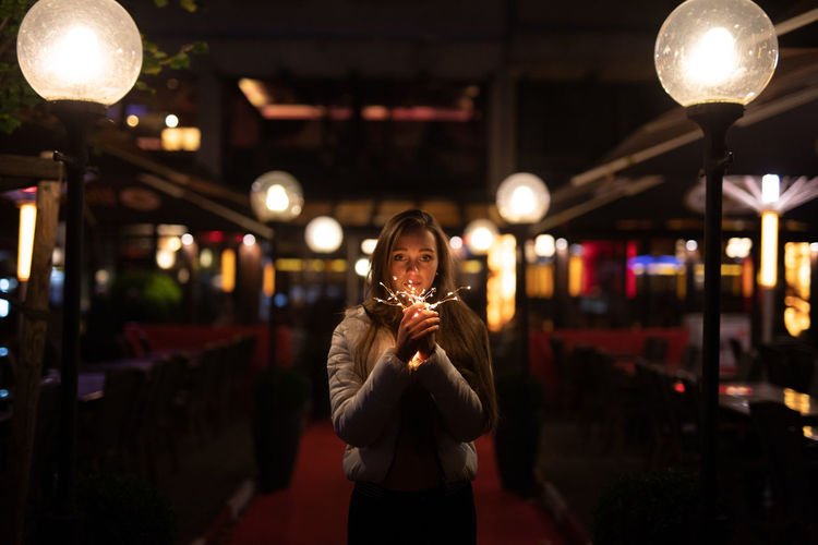 Young woman holding illuminated lighting equipment while standing at entrance of restaurant