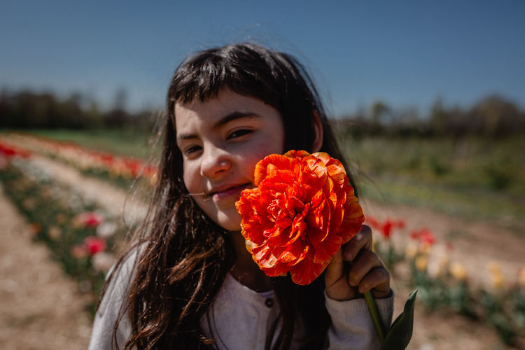 Portrait of girl holding big orange tulip in colorful flower field