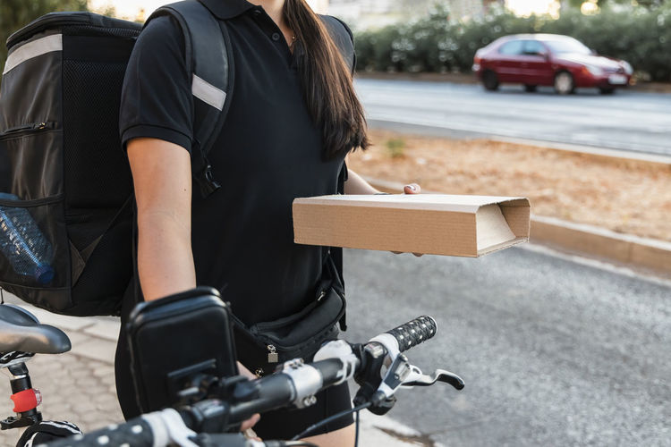 Female essential worker holding courier package while wheeling cycle