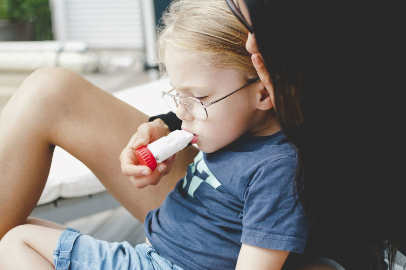 Mother examining sick son with equipment at yard