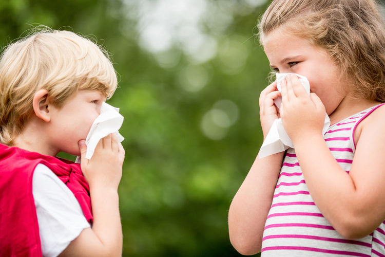 Siblings blowing noses while standing face to face in public park