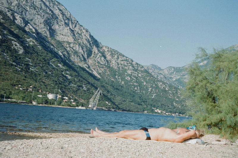 Man lying down on shore against sky