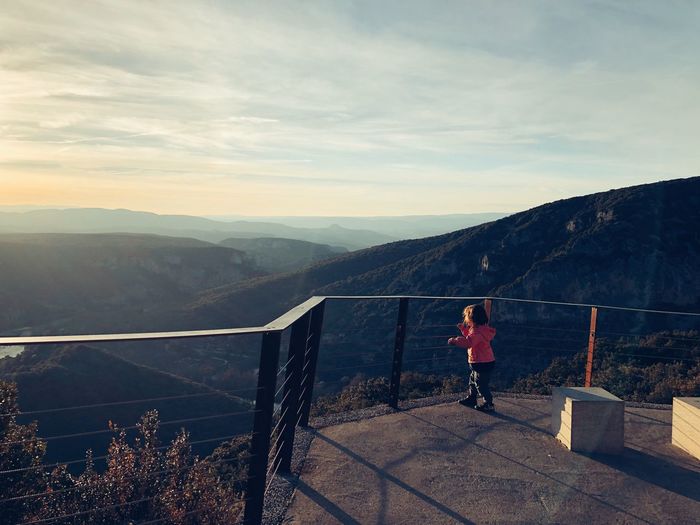 Side view of girl standing on mountain against sky during sunset