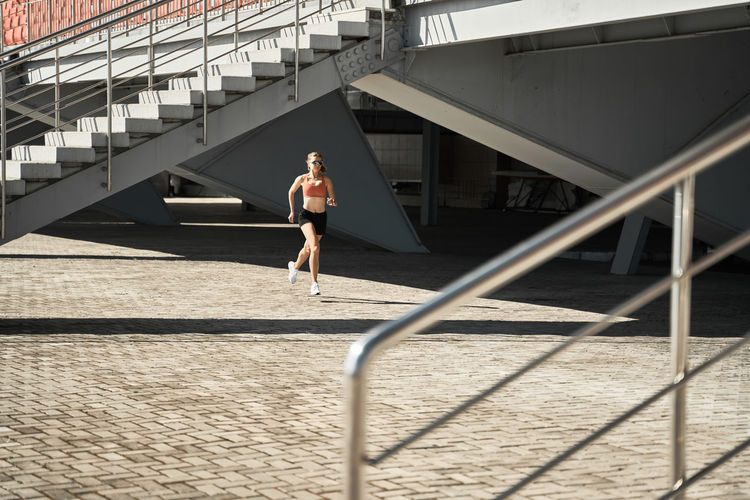 Side view of determined female athlete running fast during outdoor workout near stairways of stadium