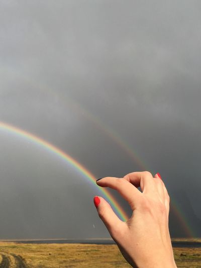Optical illusion of woman hand holding rainbow against cloudy sky