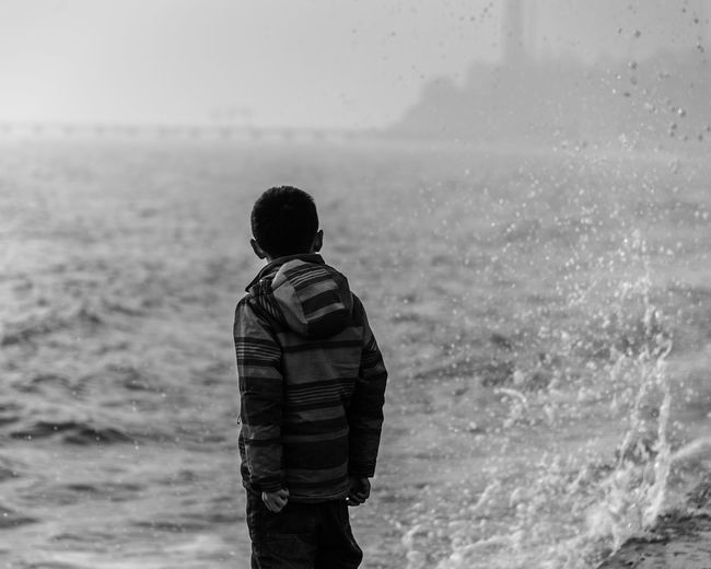 Rear view of boy standing at shore against sky