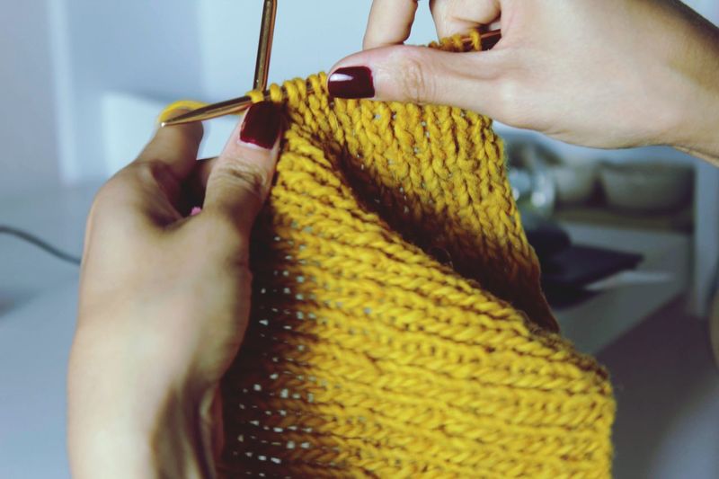 Cropped hands of woman knitting yellow fabric