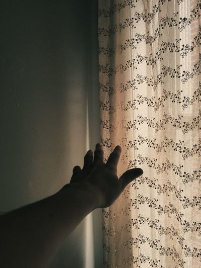 Cropped image of hand reaching curtain at home