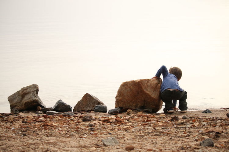 Rear view of men sitting on rock against clear sky