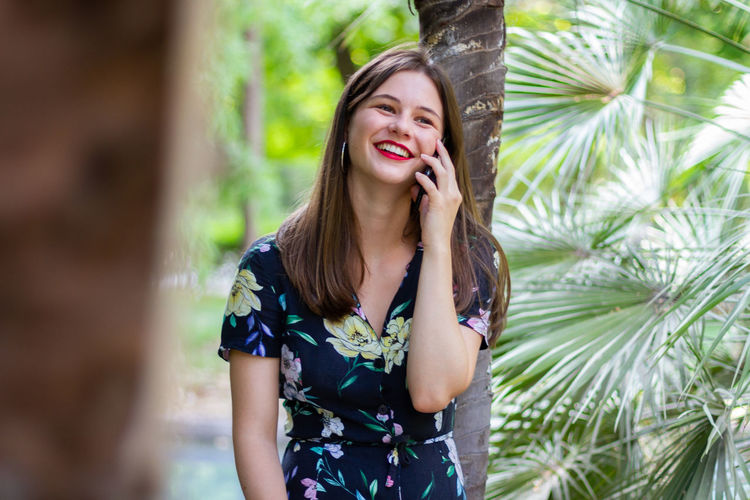 Beautiful young woman using phone while standing on plant