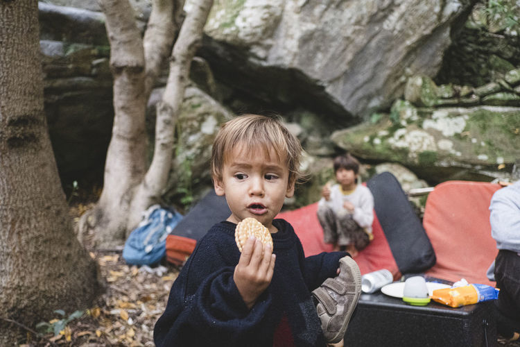 Portrait of a young kid eating a cookie at camp site in a forest