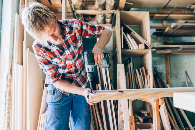 Mid adult man drilling wood in workshop