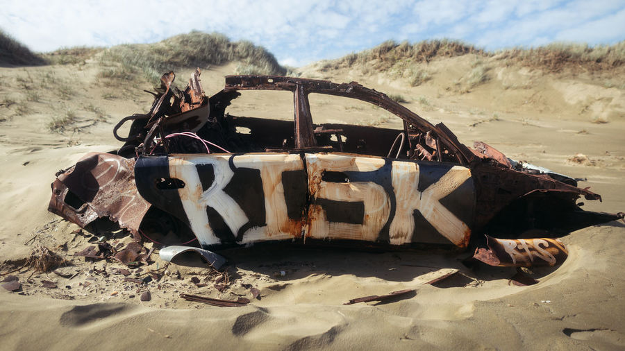 Abandoned car on sand at beach against sky