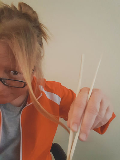 Close-up of woman holding chopsticks against wall