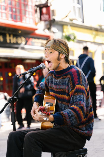 Vertical photo of a young man singing while playing guitar in the street