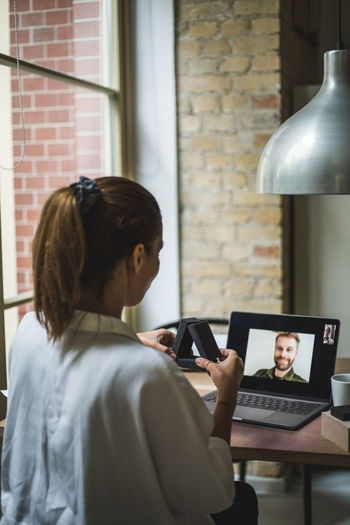 Rear view of female designer holding model while talking to coworker through video call in home office