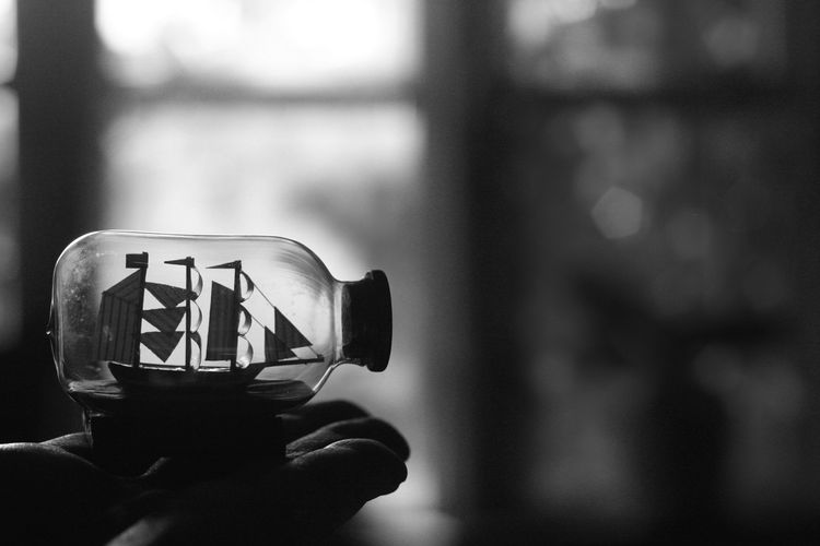 Close-up of cropped hand holding toy ship in jar