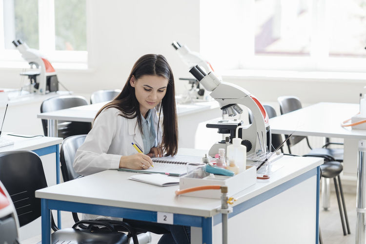 Young researcher in white coat taking notes in science class