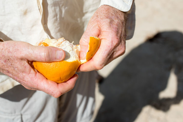 Close-up of man peeling orange outdoors