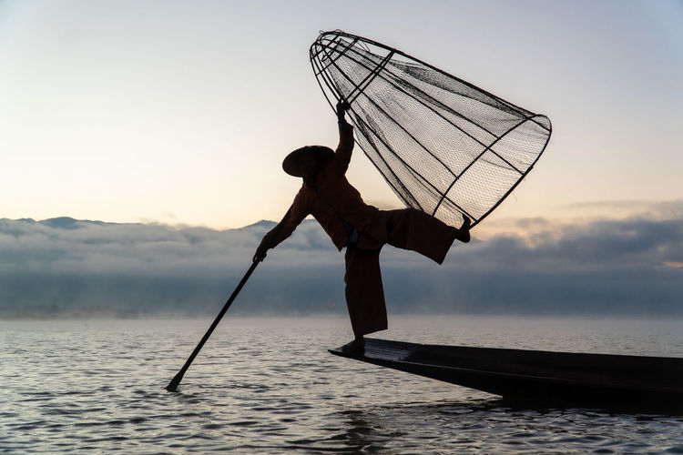Silhouette of traditional fisherman with boat on inle lake during sunrise against sky