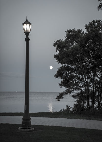 Illuminated street light by sea against clear sky at night