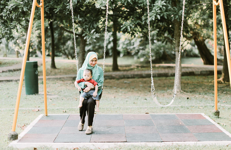 Mother holding son while swinging at playground