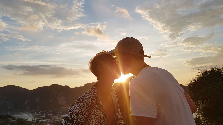 Gay men kissing against sky during sunset
