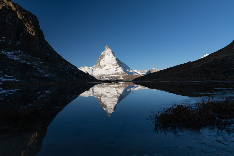 Scenic view of lake and snowcapped mountains against clear blue sky