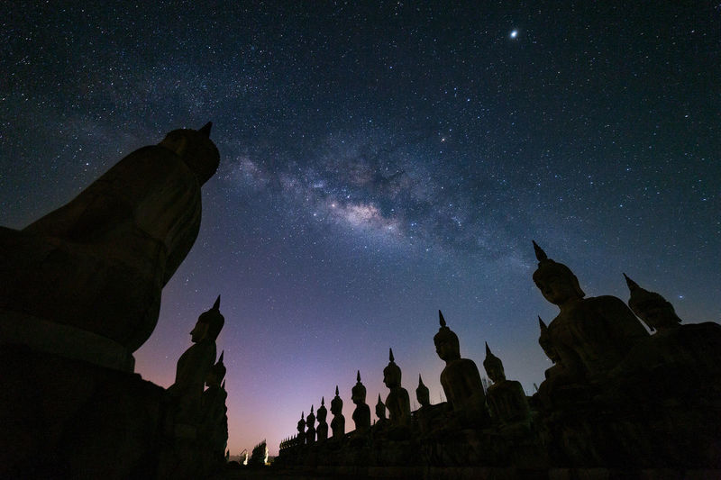 Low angle view of buddha statues against star field at night