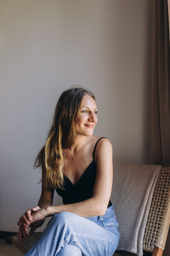 Portrait of woman looking away, sitting on a chair by the window 