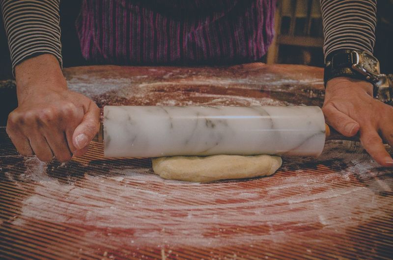 Cropped image of woman rolling dough in kitchen