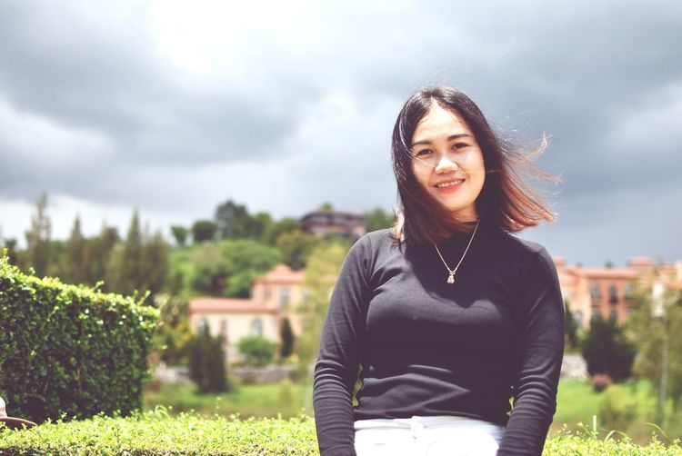 Portrait of smiling young woman standing against sky