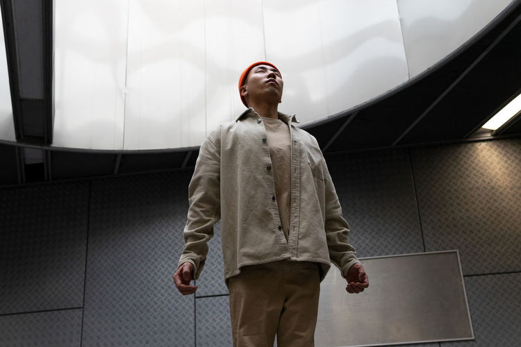 Focused stylist asian male wearing casual outfit levitating with eyes closed above floor in building hallway