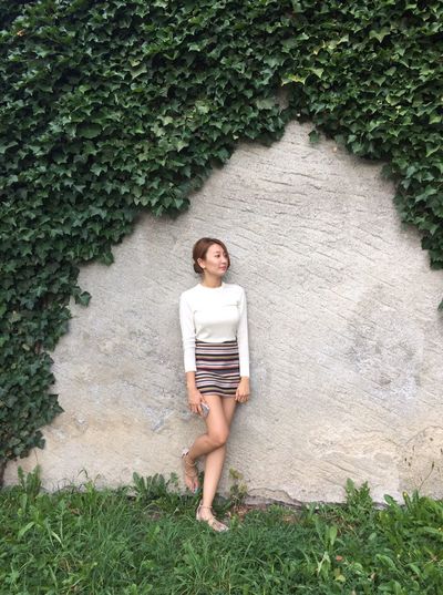 Young woman standing against wall with ivy