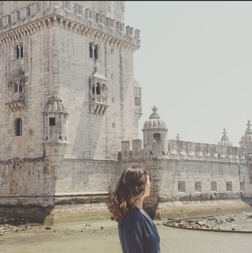 Side view of woman standing by torre de belem against clear sky