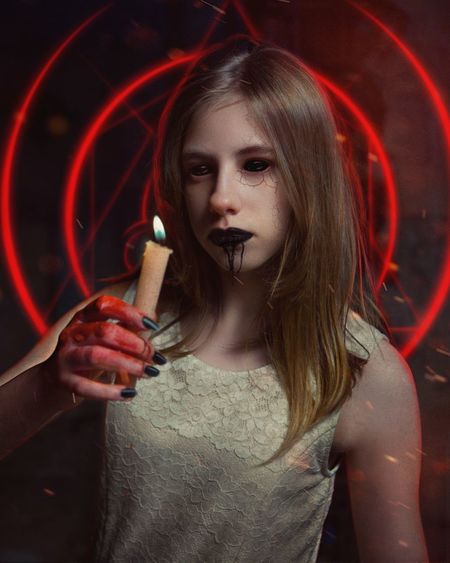Close-up portrait of young woman wearing spooky make-up while holding lit candle