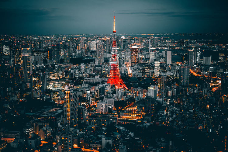 Illuminated tokyo tower amidst buildings in city against sky