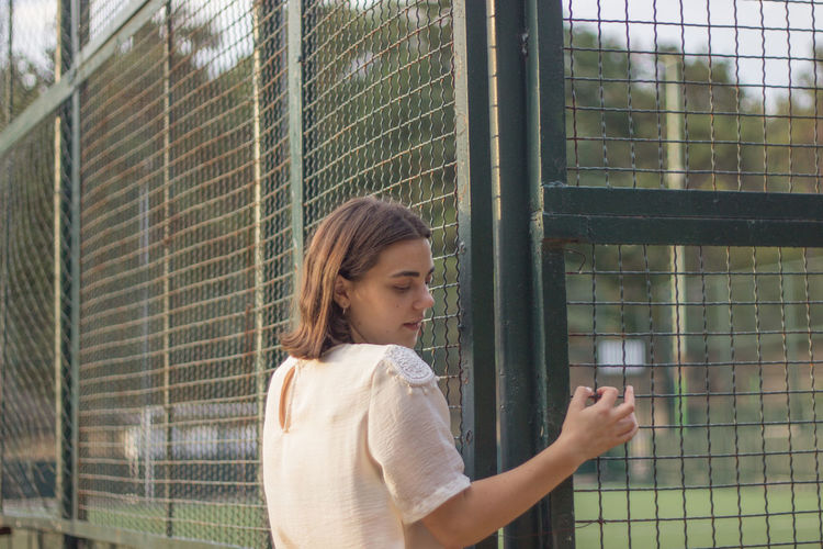 Young woman looking through window while standing on fence