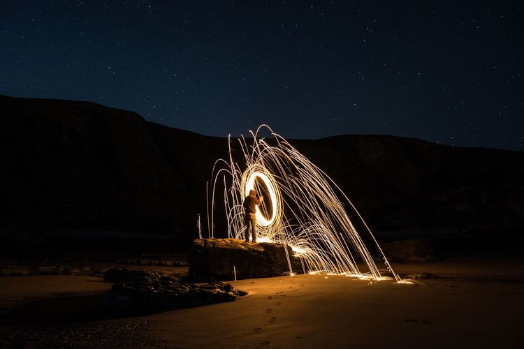 Man standing by wire wool at beach against sky