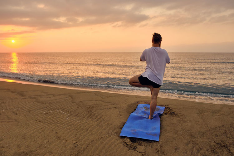 Man stands balancing in tree pose asana at beach during sunrise. yoga practices. getting balance